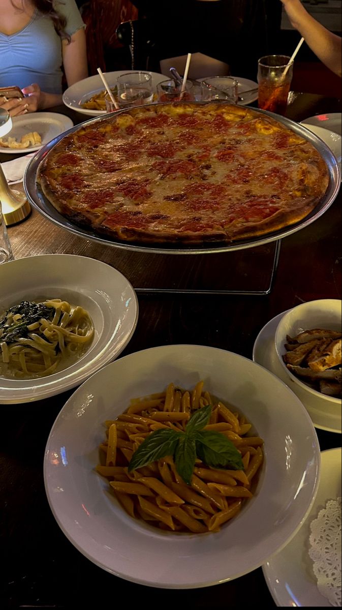 a large pizza sitting on top of a table next to plates of pasta and olives