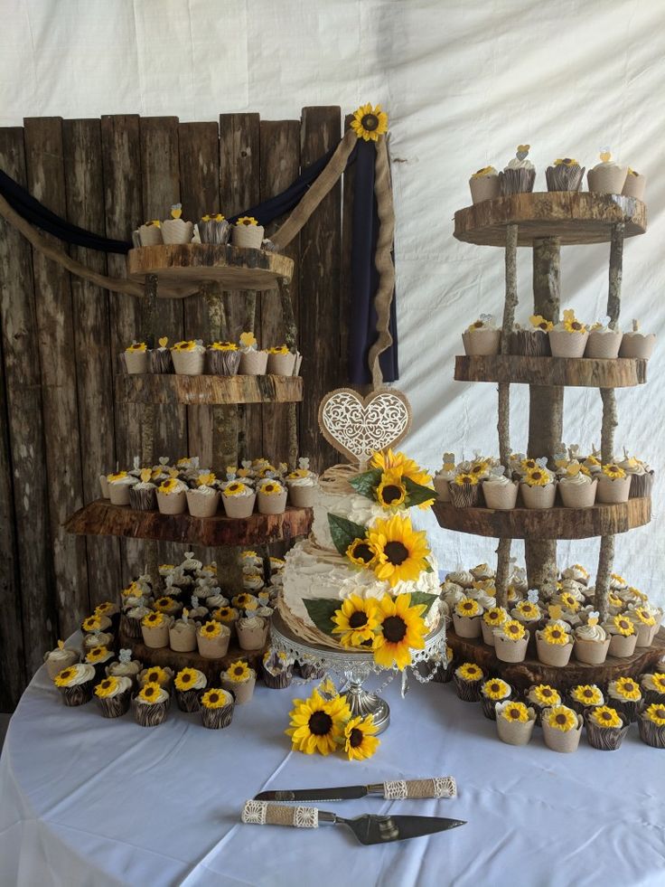 a table topped with lots of cupcakes and sunflowers