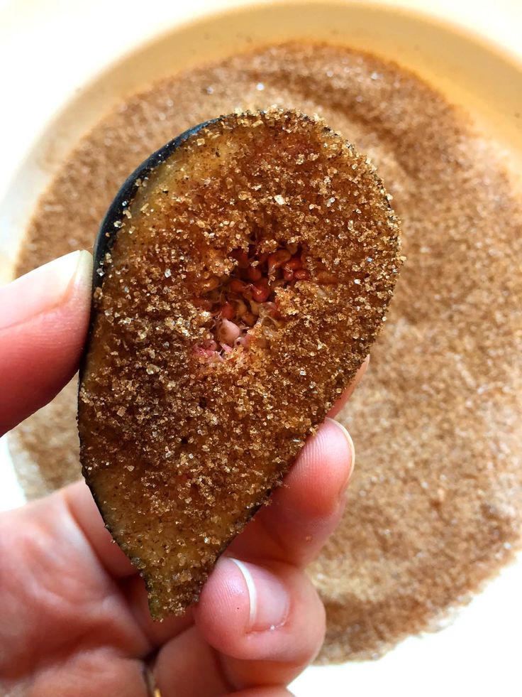 a person holding up a piece of food in front of a bowl filled with brown stuff