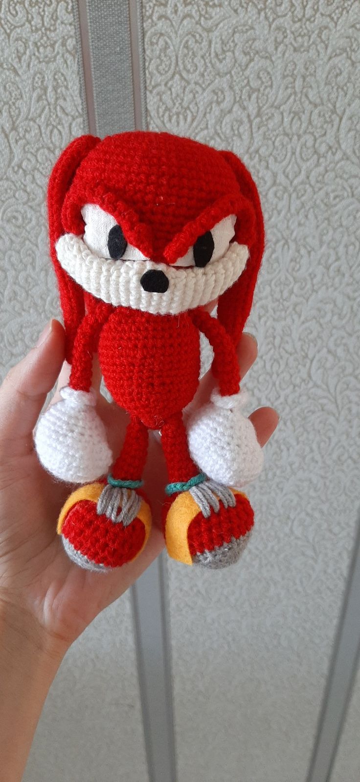 a hand holding a crocheted red and white stuffed animal