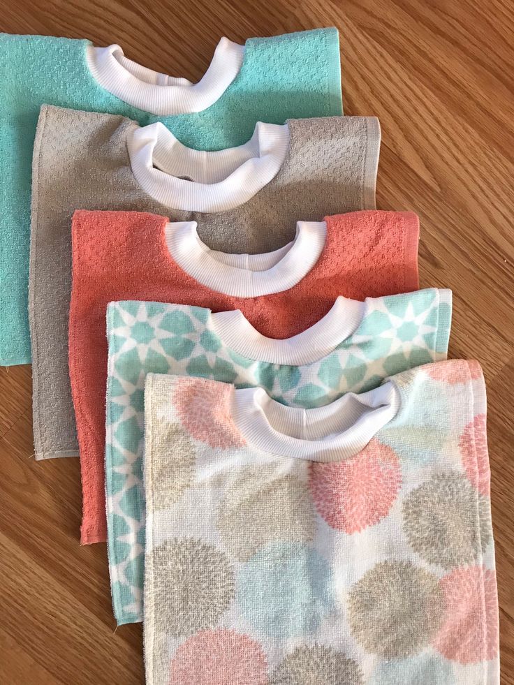 four baby bibs laying on top of a wooden floor next to each other,