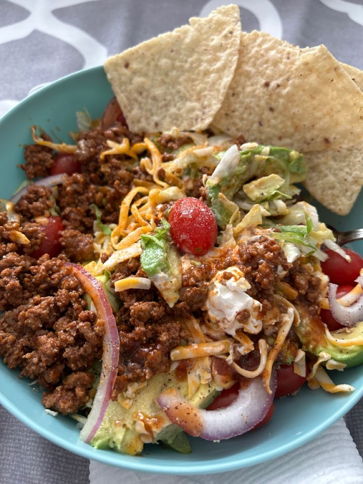 a blue bowl filled with taco salad and tortilla chips on top of a table