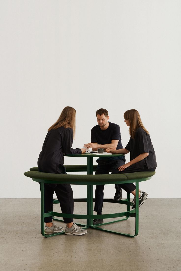 three people sitting at a green table with one person on the other side playing cards