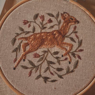 an embroidered deer with leaves on it's back is sitting in front of a wooden hoop