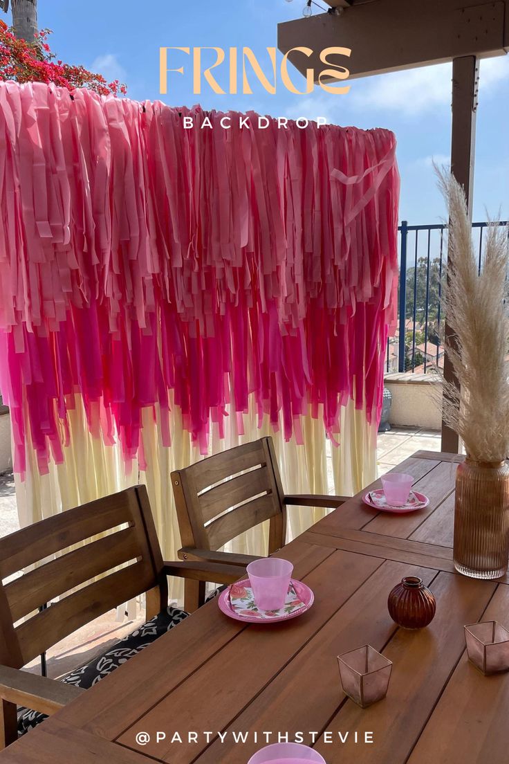 a wooden table topped with plates and pink napkins next to a vase filled with flowers