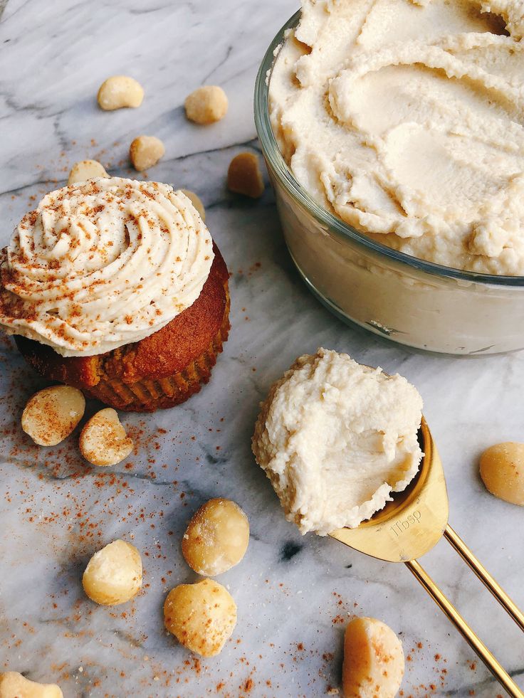 two cupcakes with frosting and nuts on a marble countertop next to a bowl of peanut butter