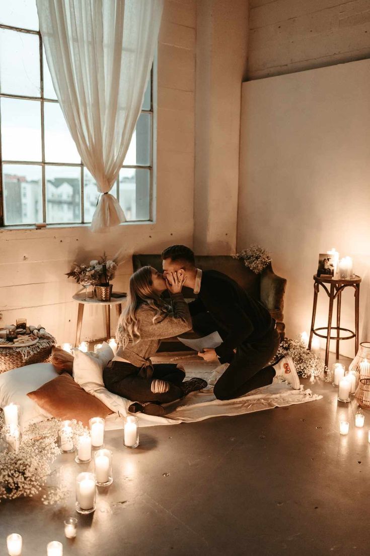 a man and woman sitting on a couch surrounded by candles in front of a window