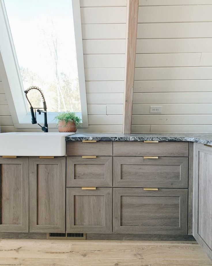 a kitchen with wooden cabinets and a white sink under a window next to a wood floor