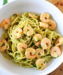 pasta with shrimp and pesto in a white bowl on top of a wooden table