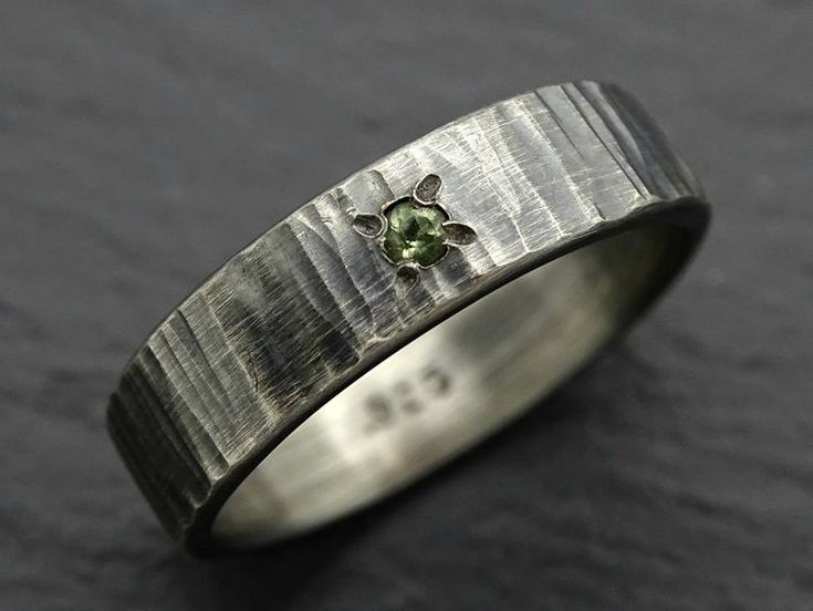 a close up of a ring with a green stone in it on a black surface