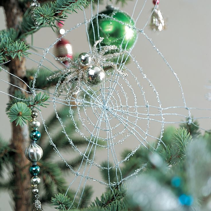 a spider web ornament hanging from a pine tree with beads and baubles