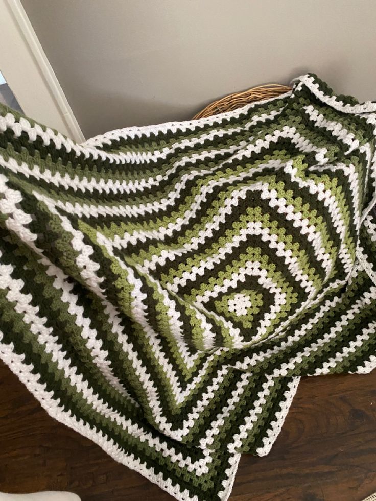 a green and white crocheted blanket sitting on top of a wooden floor next to a chair