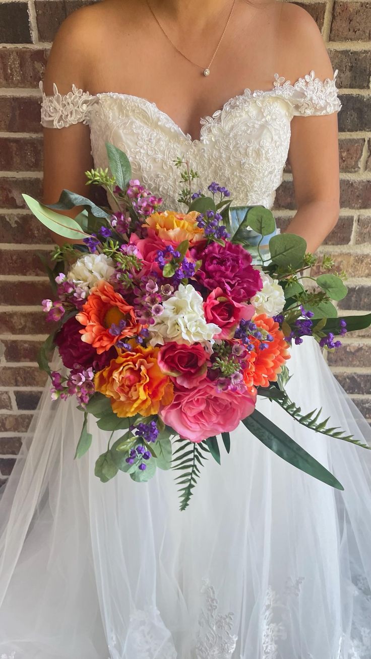 a woman in a wedding dress holding a large bouquet of colorful flowers and greenery