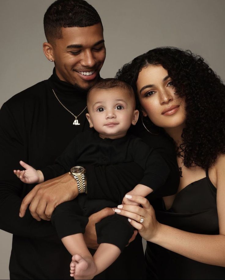 a man and woman holding a baby in front of a gray background with the child's name on it