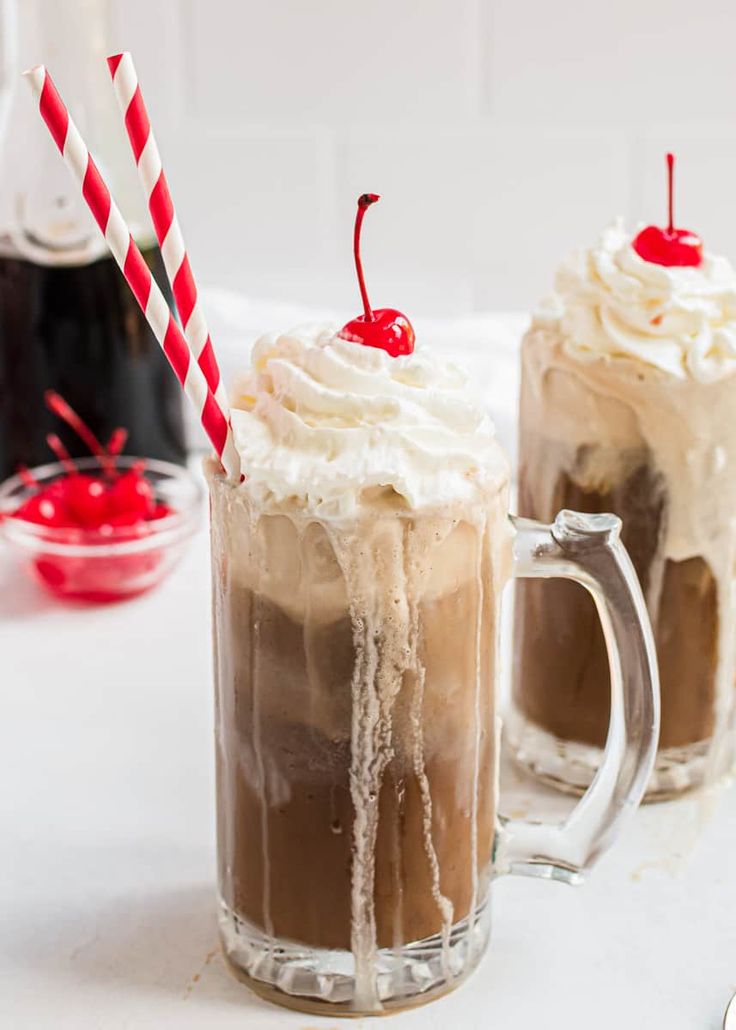 two mugs filled with ice cream and topped with whipped cream, chocolate pudding and cherries