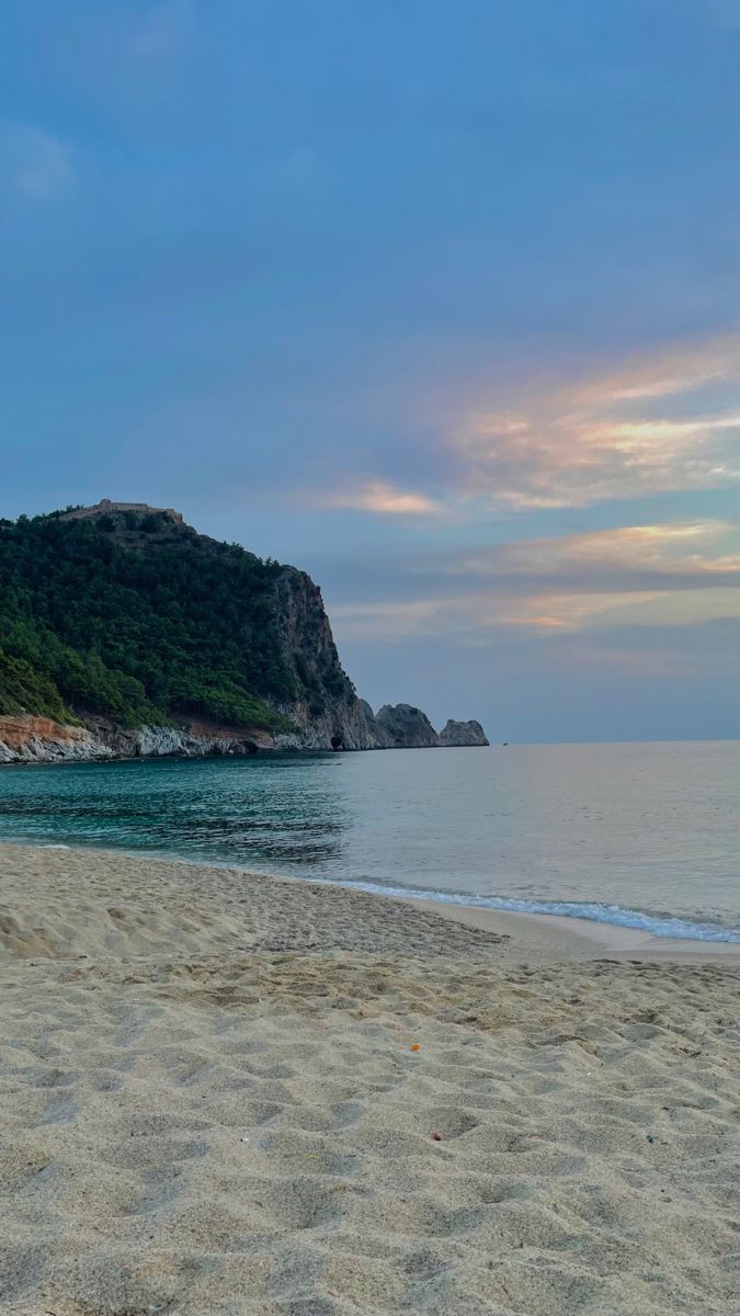 an empty beach next to the ocean with a mountain in the background at sunset or dawn