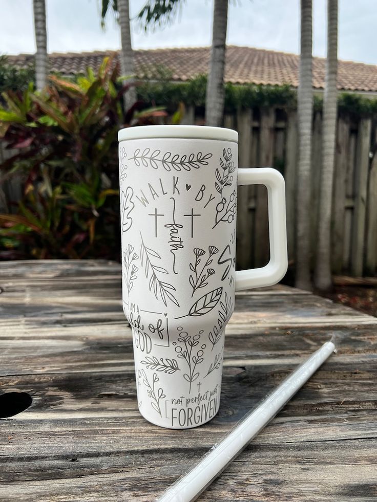 a white coffee cup sitting on top of a wooden table next to a palm tree