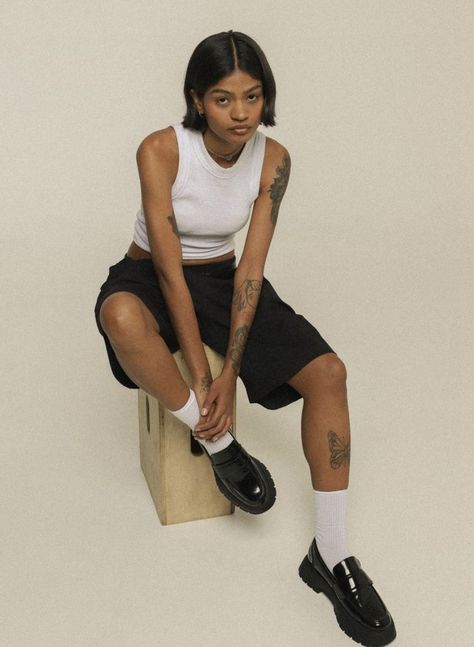 a woman sitting on top of a wooden block wearing black shoes and white tank top