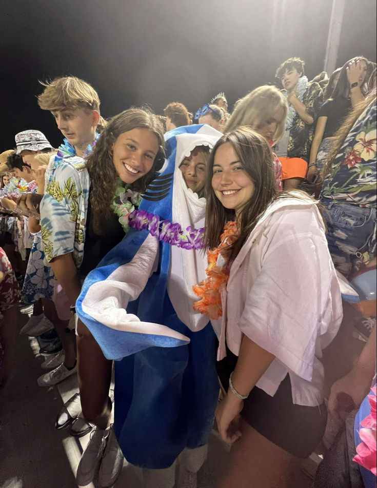 two young women standing next to each other in front of a group of people wearing leis