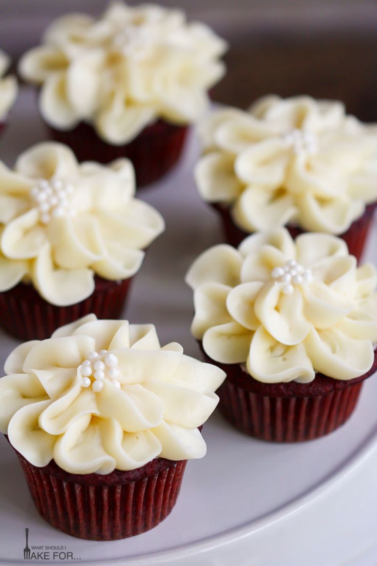 some cupcakes with white frosting and flowers on top are sitting on a plate