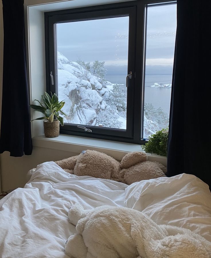 an unmade bed in front of a window with snow on the ground and mountains outside