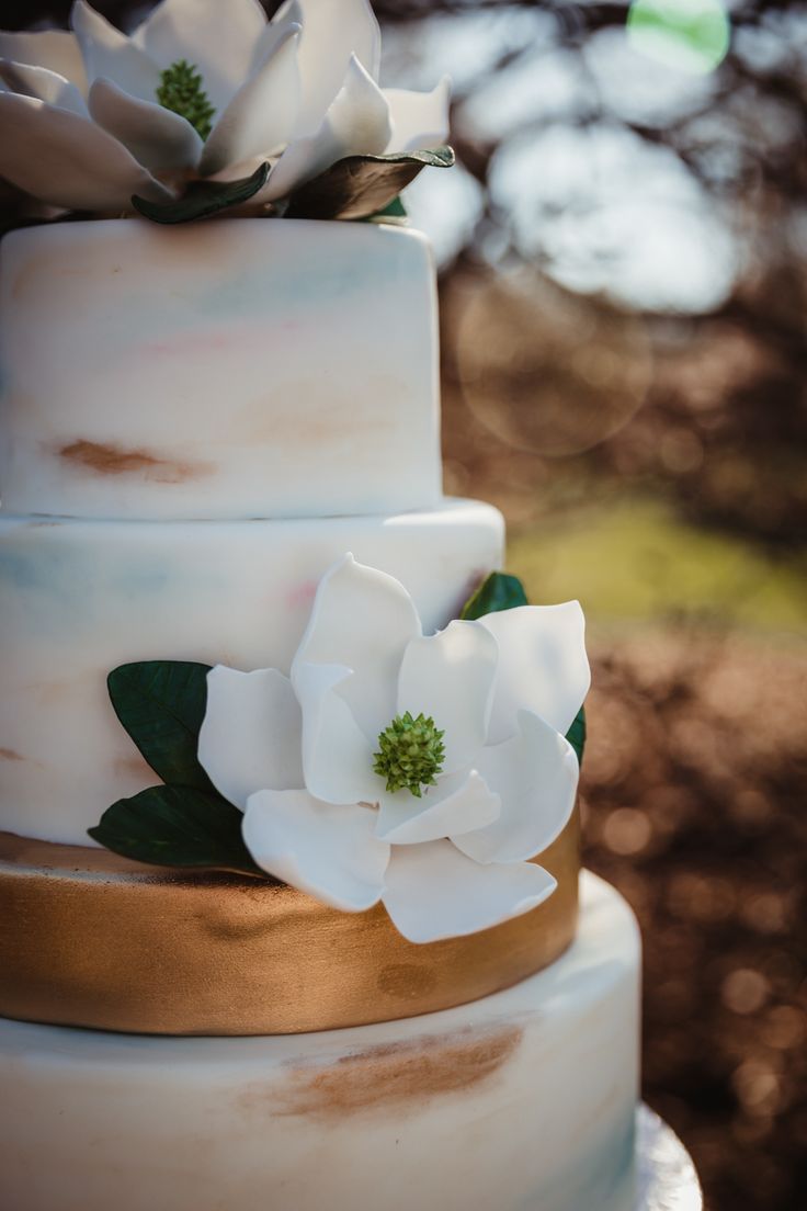 a three tiered cake with white flowers on top and gold trim around the edges