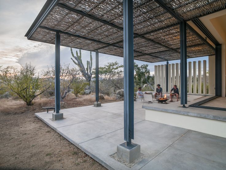 two people sitting on a porch under a covered area with cactus in the background at sunset