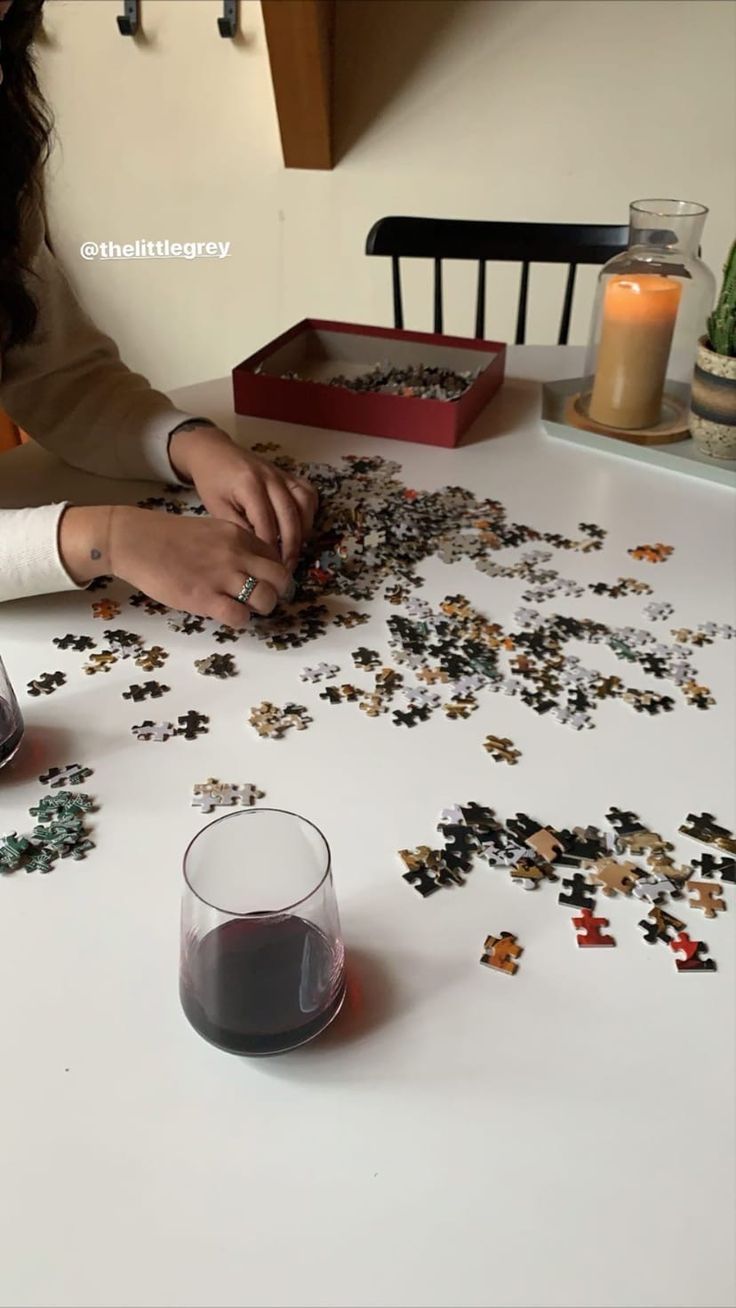 a woman sitting at a table with a glass of wine and puzzle pieces on it