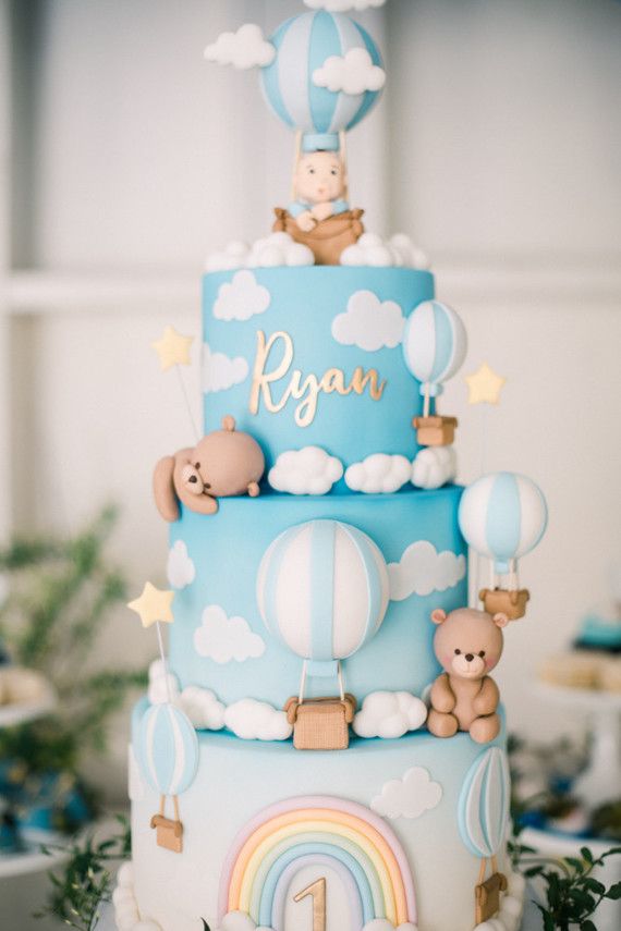 a blue and white cake with bears on top, hot air balloons in the sky