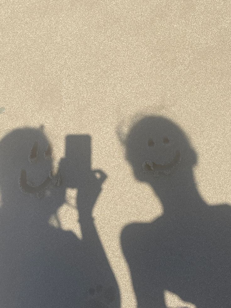 the shadow of two people holding up their cell phones in front of them, with one person taking a photo