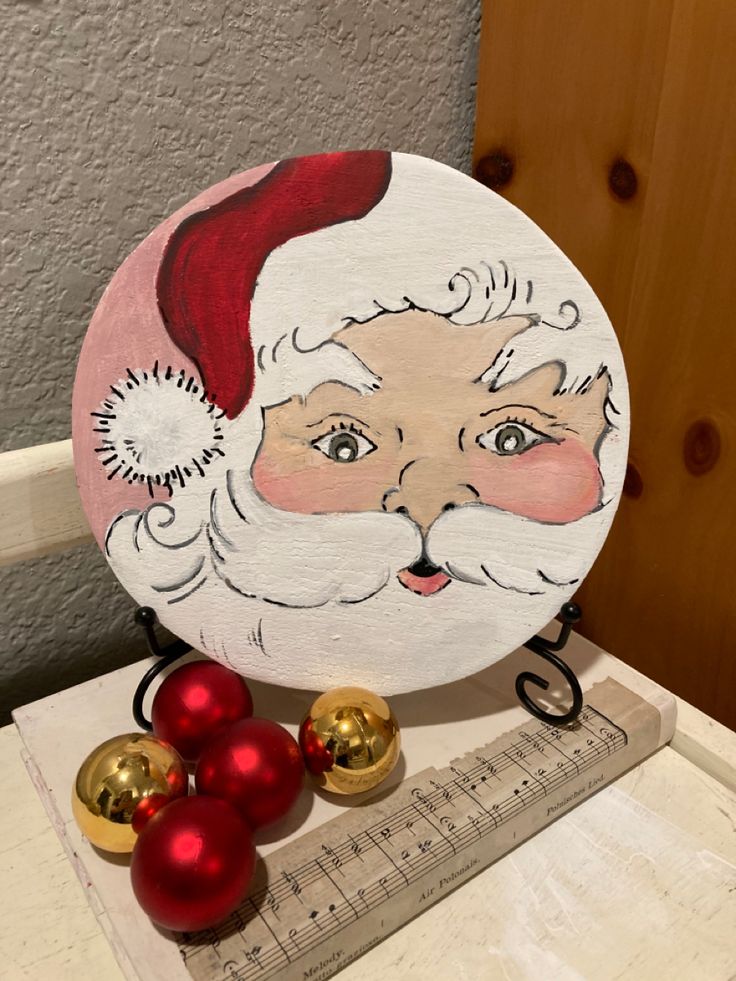 a wooden plate with a santa face painted on it next to christmas ornaments and a ruler