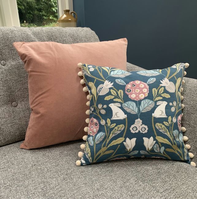 a blue and pink pillow with pom - poms on it sitting on a couch