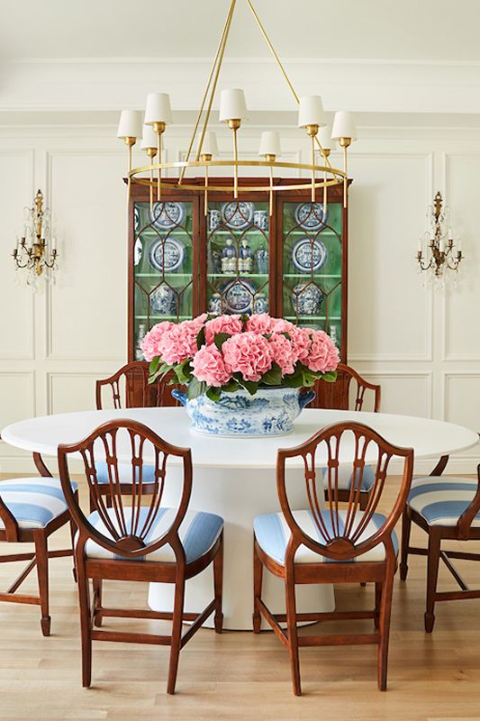 a dining room table with four chairs and a vase of flowers on the table in front of two windows