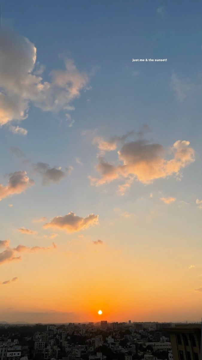 the sun is setting over a city with buildings in the foreground and clouds in the background