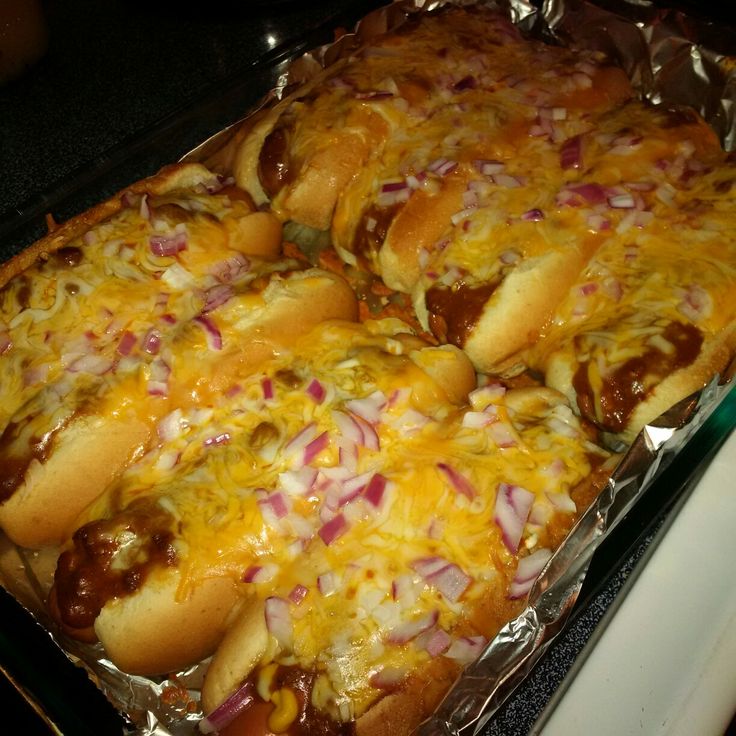 hotdogs covered in cheese and onions on top of aluminum foil lined baking pan