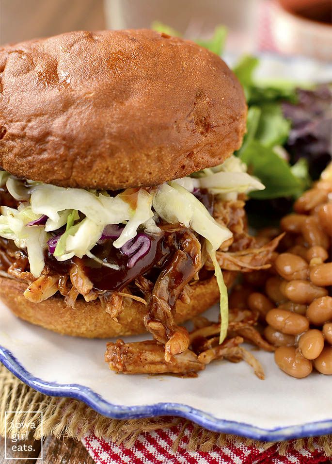 a pulled pork sandwich with coleslaw, beans and lettuce on a plate