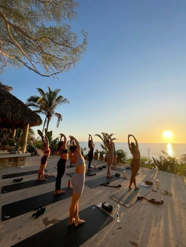 a group of people doing yoga on top of a roof next to the ocean at sunset