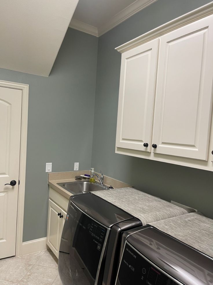 an empty laundry room with two washers and dryer in the foreground, next to a sink