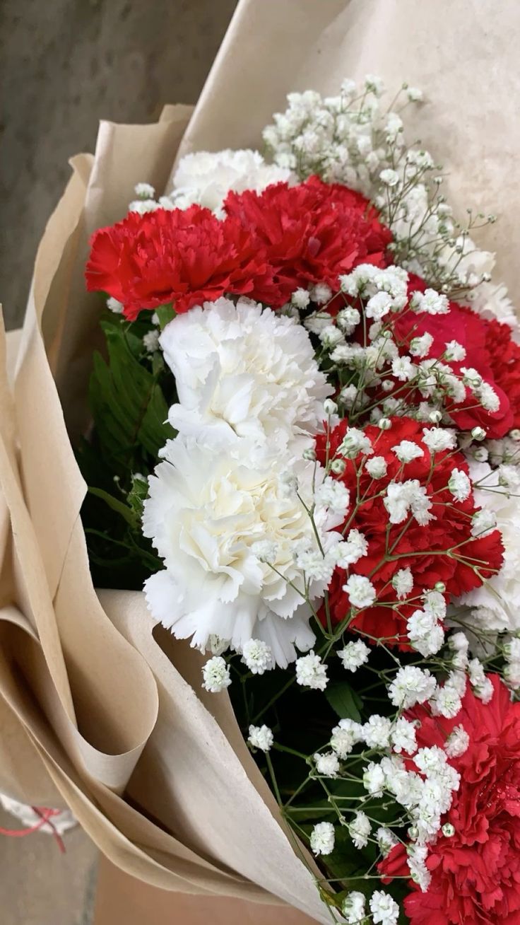 red and white carnations are in a bouquet on the floor next to brown paper