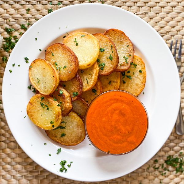 a white plate topped with potato wedges next to a small bowl of tomato sauce