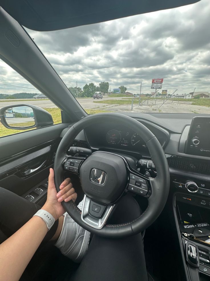 a woman is driving her car on the road with an overcast sky in the background