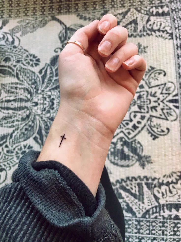 a woman's wrist with a small cross tattoo on the left side of her arm