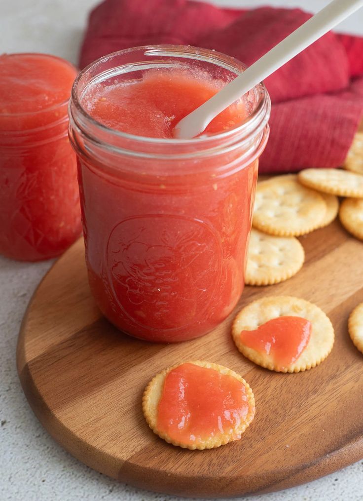 a jar filled with jelly next to crackers on a cutting board