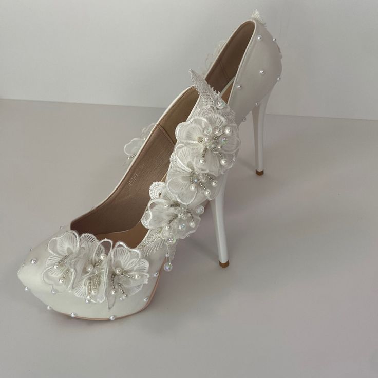 a pair of white high heel shoes with flowers on the side and pearls at the toe