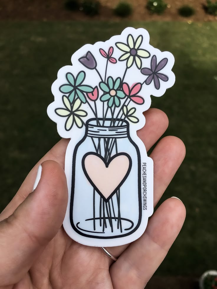 a hand holding a sticker with flowers in a mason jar