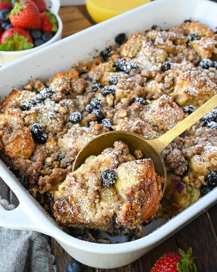 a casserole dish with blueberries, strawberries and orange juice in the background