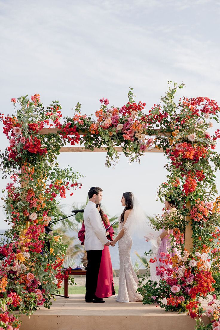 a bride and groom standing under an arch with flowers on it at the end of their wedding ceremony