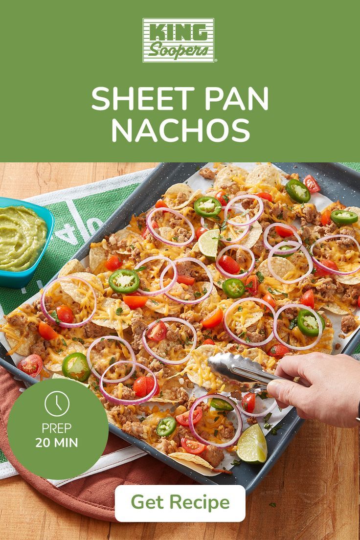 a sheet pan filled with nachos on top of a wooden table next to guacamole