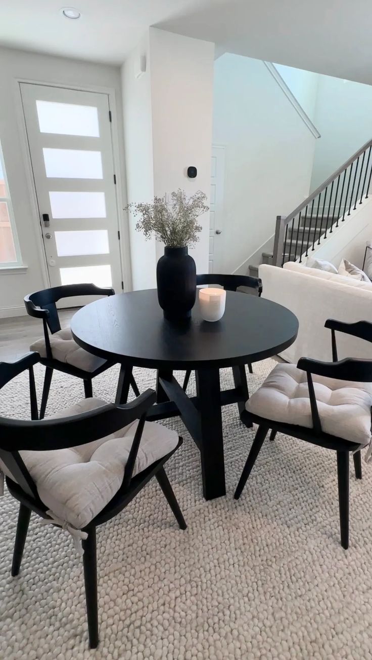 a table with chairs and a vase on top of it in front of a stair case