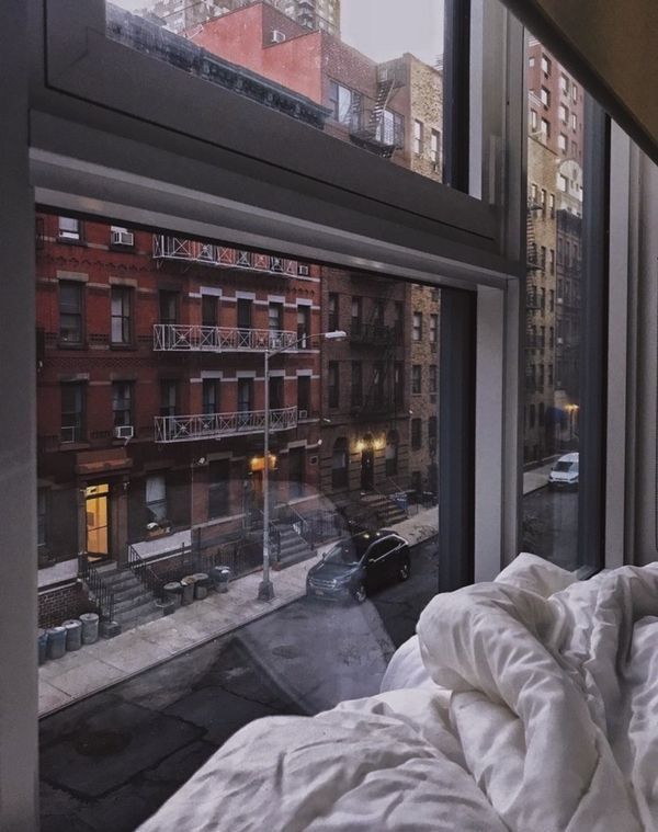 an unmade bed sitting in front of a window next to a tall building with lots of windows